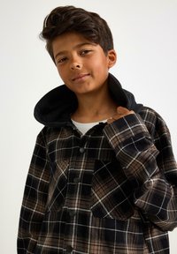 Sort og brun skotsk ternet flanneljakke med sort hætte, der har en knaplukning foran, kontrasterende hvide detaljer og to forlommer.