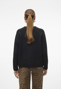 Schwarzer, strukturierter Pullover mit rundem Hals und Raglanärmeln, kombiniert mit einer Hose im Leopardenmuster, von hinten gezeigt mit langen, glatten Haaren.