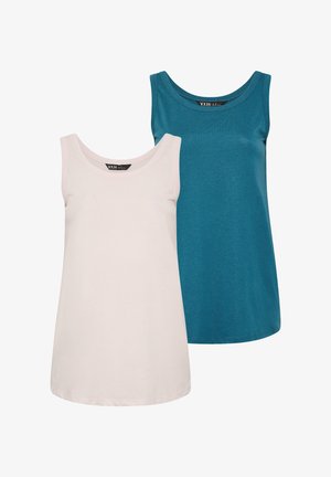 Donna bionda che indossa un top verde acqua senza maniche con spalline larghe, jeans azzurri a gamba larga e sneakers bianche, in piedi su uno sfondo chiaro.