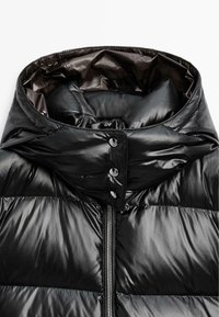 Black puffer jacket featuring a high collar, glossy texture, prominent quilting, and a central zip with snap-button closures.