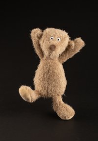 Stuffed bear in light brown plush with short, shaggy fur, wide-set eyes, a round nose, and limbs raised in a playful pose.