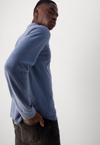 Chemise en coton bleu à manches longues avec une coupe classique, dotée d'un col rond et de détails de couture subtils, associée à un jean sombre.