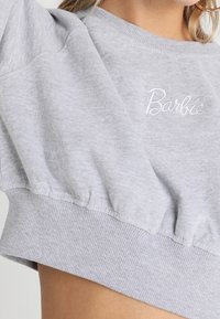 Felpa corta grigio chiaro con orlo elasticizzato e maniche a sbuffo. Presenta il logo "Barbie" ricamato in bianco sul davanti.