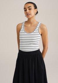 Top in bianco a righe navy, abbinato a una gonna nera fluida. Il top ha uno scollo a barca e un materiale leggermente texturizzato.