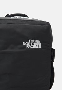 Musta reppu, jossa on teksturoitu kangas, varustettuna heijastavalla "THE NORTH FACE" -logolla ja yläkahvalla kantamista varten.