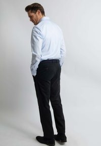 Lichtblauw overhemd met lange mouwen, zwarte broek en zwarte schoenen. Het overhemd heeft een kraag, knopen en opgerolde mouwen, de broek heeft een rechte pasvorm.