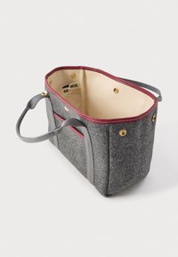 Pelēka auduma somiņa ar tumši sarkanu apdari, gaiši brūnu iekšpusi, zelta spiedpogu, ārējo kabatu un divām auduma rokturiem.