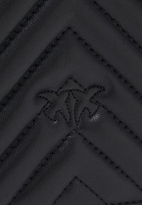 Zwart leren stof met een gestikt patroon en zichtbare stiksels. Bevat een klein, gecast logo in het midden. Glad textuur.