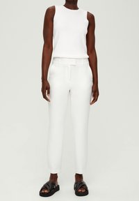 White sleeveless top and tailored white trousers with a belted waist, paired with black strappy sandals. Smooth, lightweight fabric.