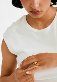 Kuldne sõrmus kõveriku kujundusega, millel on kaks siledat helmestikest, kantud käsel, mille küüned on hoolikalt kujundatud, heleda tausta taustal.