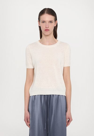 Pull en crème clair à manches courtes en maille, avec un col rond et une coupe légèrement décontractée. Associé à un pantalon en satin gris.