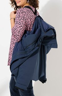Giubbotto a strati blu navy con cerniere e cinturini regolabili. Indossato sopra una maglietta rosa con stampa leopardo. Tessuto testurizzato, design minimalista.