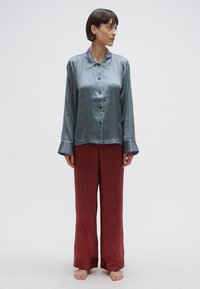 Jedwabista, ciemnoniebieska piżama na guziki z subtelnym wzorem i kontrastującym białym obszyciem; w połączeniu z luźnymi, czerwonymi spodniami w wzory.