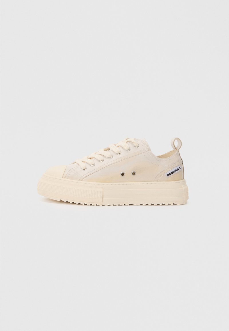 Beige canvas sneakers with a round toe, lace-up design, and a textured rubber sole. Features small ventilation holes and a heel tab.