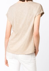 Beige krátký rukáv top s kulatým výstřihem, měkkou texturou a ohrnutými rukávy, doplněný bílými džíny. Jednoduchý a ležérní design.