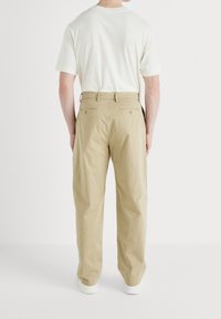 Beige katoenen broeken met een relaxte pasvorm, voorzien van twee achterzakken en een riemlus. Gestyled met een wit T-shirt met ronde hals.