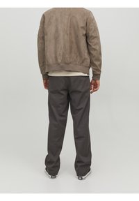 Bruine suède bomberjack met ribgebreide boorden, gedragen over een lichte T-shirt en gecombineerd met donkergrijze, relaxed-fit broek en zwarte sneakers.