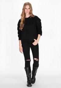 Sort oversized sweater med struktureret strik, parret med sorte ripped skinny jeans og knæhøje sorte støvler med spænder.