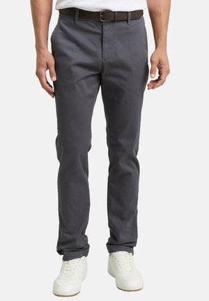 Pantalon pour homme en mélange de coton gris, coupe droite, design à 5 poches, fermeture à boutons, associé à une ceinture marron et des baskets blanches.