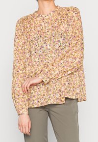 Blusa floreale gialla con motivi viola e rosa, maniche lunghe, scollatura rotonda e dettagli con bottoni. Tessuto morbido con vestibilità comoda.