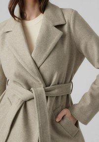 Beige wolmix jas met een sjawl-kraag, wikkelontwerp, zelfbindriem en zijzakken. Zachte textuur met minimale stikdetails.