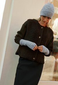 Braune Strickjacke mit strukturiertem Finish, graue gerippte Handschuhe und eine graue Strickmütze. Die Knopfdetails an der Jacke sind sichtbar.