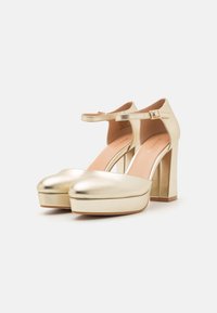 Gold metallic high-heeled shoes with a thick platform and ankle strap. Smooth texture, rounded toe, and square block heel design.