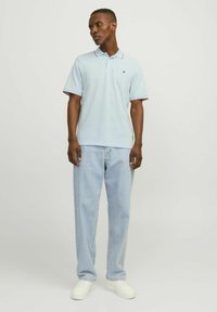 Polo shirt azzurro chiaro con rifiniture rosse, abbinato a jeans azzurro chiaro a gamba dritta e sneakers bianche. Design semplice con dettaglio del logo ricamato.