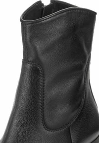 Primer plano de una bota de cuero negro hasta el tobillo con paneles texturizados y lisos, destacando la costura y un cremalleras lateral.