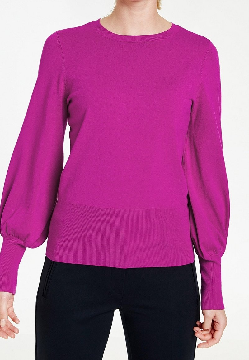 Fuchsia stickad tröja med långa, ballongsärmar och ribbad nederdel. Tyget är slätt med en något elastisk struktur.