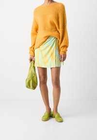 Suéter amarillo esponjoso, mini falda de mármol azul y amarillo, bolso de cuero verde y mocasines a juego con tacón cuadrado.