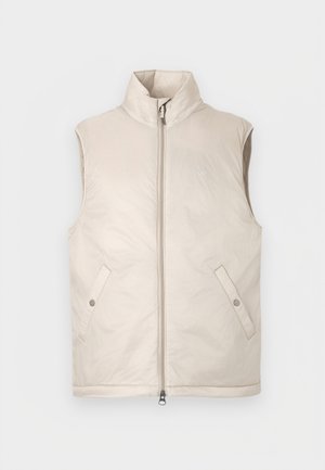 Chaleco acolchado sin mangas en color beige con cuello alto, cremallera frontal y dos bolsillos laterales, con una textura suave y diseño minimalista.