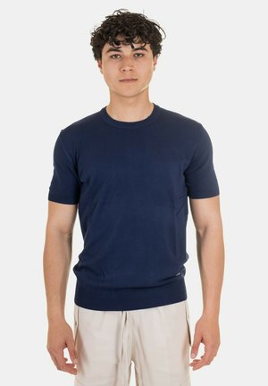 Maglietta a maniche corte in maglia di colore blu navy con scollatura rotonda e orlo a coste. Texture liscia, design aderente, indossata con pantaloni corti di colore chiaro.