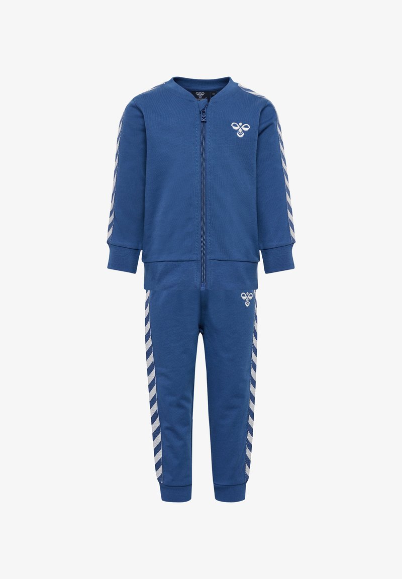 Survêtement bleu royal composé d'une veste zippée et d'un pantalon assorti. Présente des rayures blanches en diagonale sur les manches et les côtés, fabriqué en tissu doux.