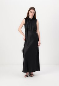 Black satin maxi dress with a high neckline and sleeveless design. Features a gathered waist and flowing skirt. Model holding a small silver purse.