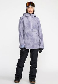 Paars tie-dye snowboardjack met ritssluiting, verstelbare capuchon en een voorzak. Zwarte sneeuwbroek en handschoenen maken de outfit compleet.