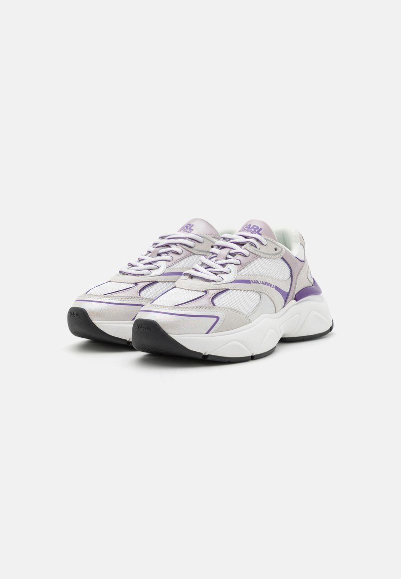 Zapatillas de cordones con un upper de malla gris y blanco, acentos morados y una suela blanca gruesa con detalles texturizados.
