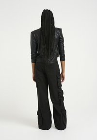 Schwarze Lederjacke mit strukturierten Schultern, kombiniert mit lockeren schwarzen Cargo-Hosen mit Seitentaschen und geradem Bein.
