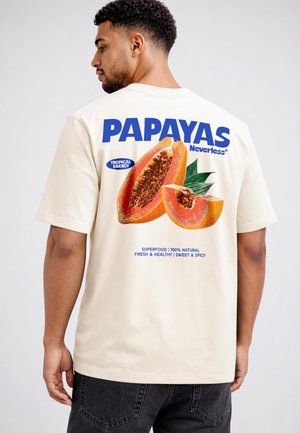 Man wearing cream t-shirt with large colorful papaya graphic and text promoting tropical energy and superfood on the back.