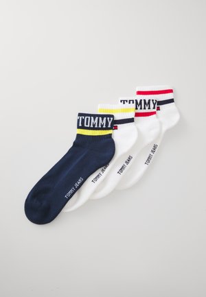 Set von vier Socken: eine marineblaue mit gelbem gestreiftem Bündchen, drei weiße mit kontrastierenden roten und gelben Bündchen, die mit "TOMMY JEANS" Branding versehen sind.