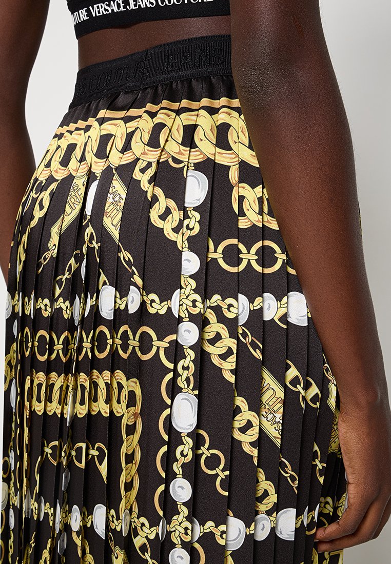 Jupe plissée noire avec des motifs en chaîne dorée et perles, dotée d'une taille élastique avec des détails de logo. Texture de tissu lisse.