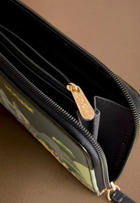 Juodas piniginė su užtrauktuku ir auksinės spalvos detalėmis, vienoje pusėje pavaizduotas grafinis dizainas, su keliais skyreliais ir lygiu tekstūruotu paviršiumi.