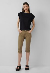 Czarny top z krótkim rękawem o szerokich ramionach, w zestawie z khaki spodniami 3/4 z podwiniętymi mankietami oraz czarnymi sandałami na platformie. Prosty i elegancki design.