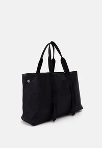 Black tote bag with a sleek design, made of smooth material. Features wide handles and a decorative silver accent on one side.