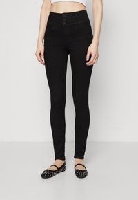 Černé skinny džíny s vysokým pasem, tříknoflíkovým zapínáním, pěti kapsami a hladkým, elastickým materiálem. V kombinaci s černými balerínami se cvočky.