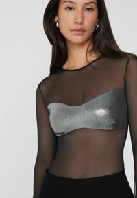 Top negro transparente de manga larga con un acento metálico plateado en el pecho, de textura suave y diseño ajustado.