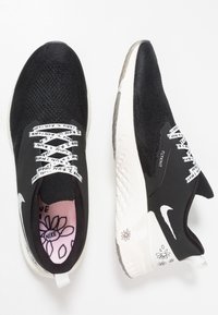 Černé tenisky s pleteným svrškem, bílou mezipodešví a ozdobnými tkaničkami. Mají vzorovanou stélku s květinovým motivem a značkovým označením Nike.