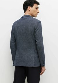 Dopasowana marynarka w ciemnoniebieskim materiale w jodełkę. Z wykładanym kołnierzem, długimi rękawami i pojedynczym rozcięciem. Posiada detale mankietów z trzema guzikami.