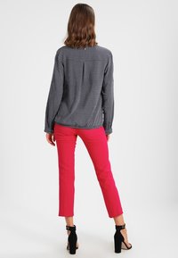Blusa a pallini blu navy con maniche lunghe, dettagli con piega sul retro, abbinata a pantaloni slim-fit rosa vivace e sandali neri con tacco.