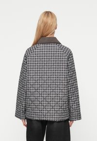 Μπουφάν καπιτονέ σε μοτίβο ασπρόμαυρου καρό, με σκούρο γιακά και φαρδιά μανίκια. Υφή υφάσματος με ελαφρώς επενδυμένη εμφάνιση.